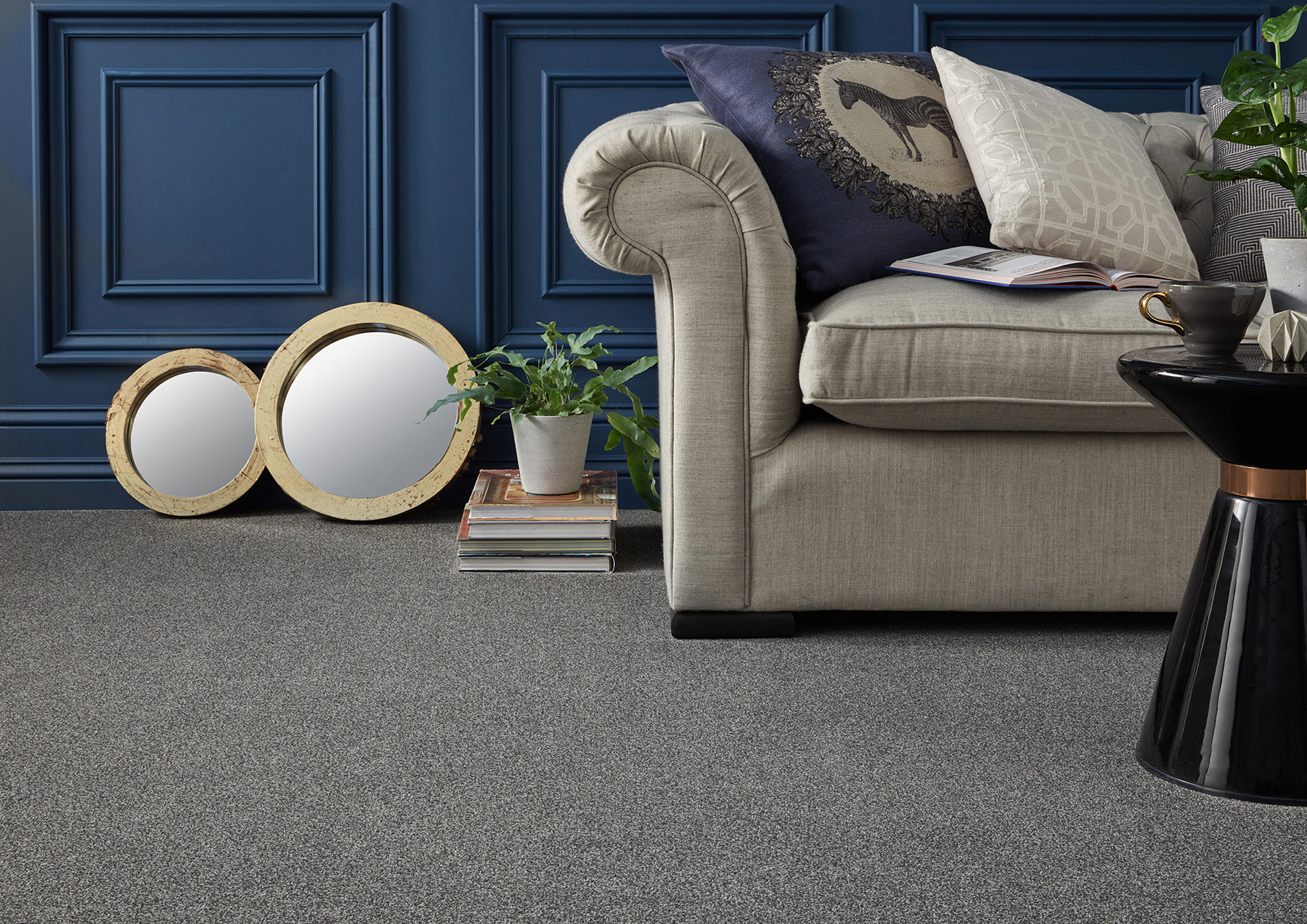 An image showing a modern living room - a deep navy wall is paired with a dark grey carpet to create an appealing and dramatic scheme. A neutral sofa provides balance for the carpet and the wall.